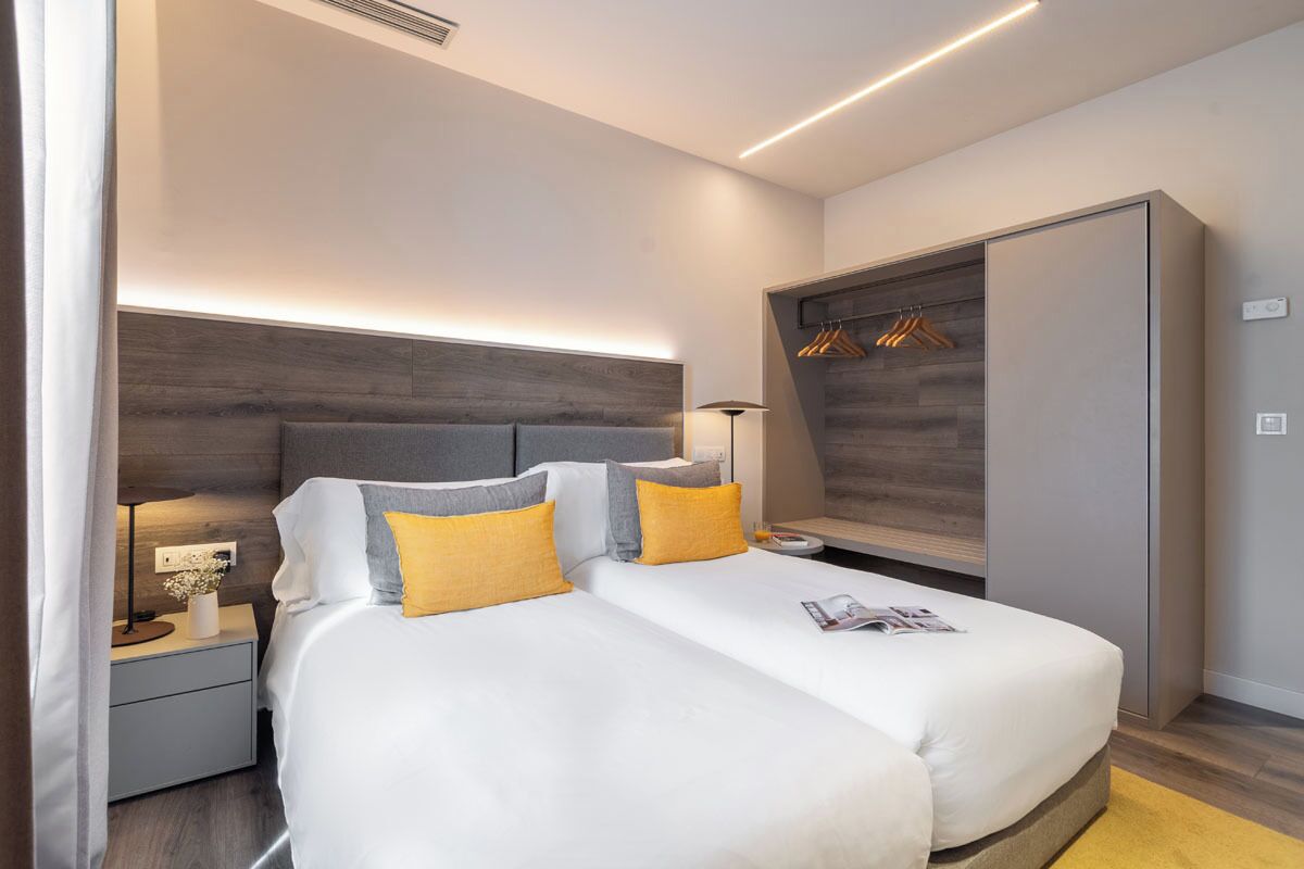 Una habitación de hotel moderna con una cama grande, mesitas de noche, un armario y un vestidor empotrado con espacio para colgar ropa.