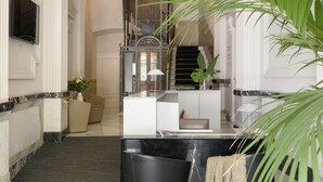 Un hall d’entrée avec un sol en marbre, un comptoir d’accueil, un escalier et une grande plante en pot.