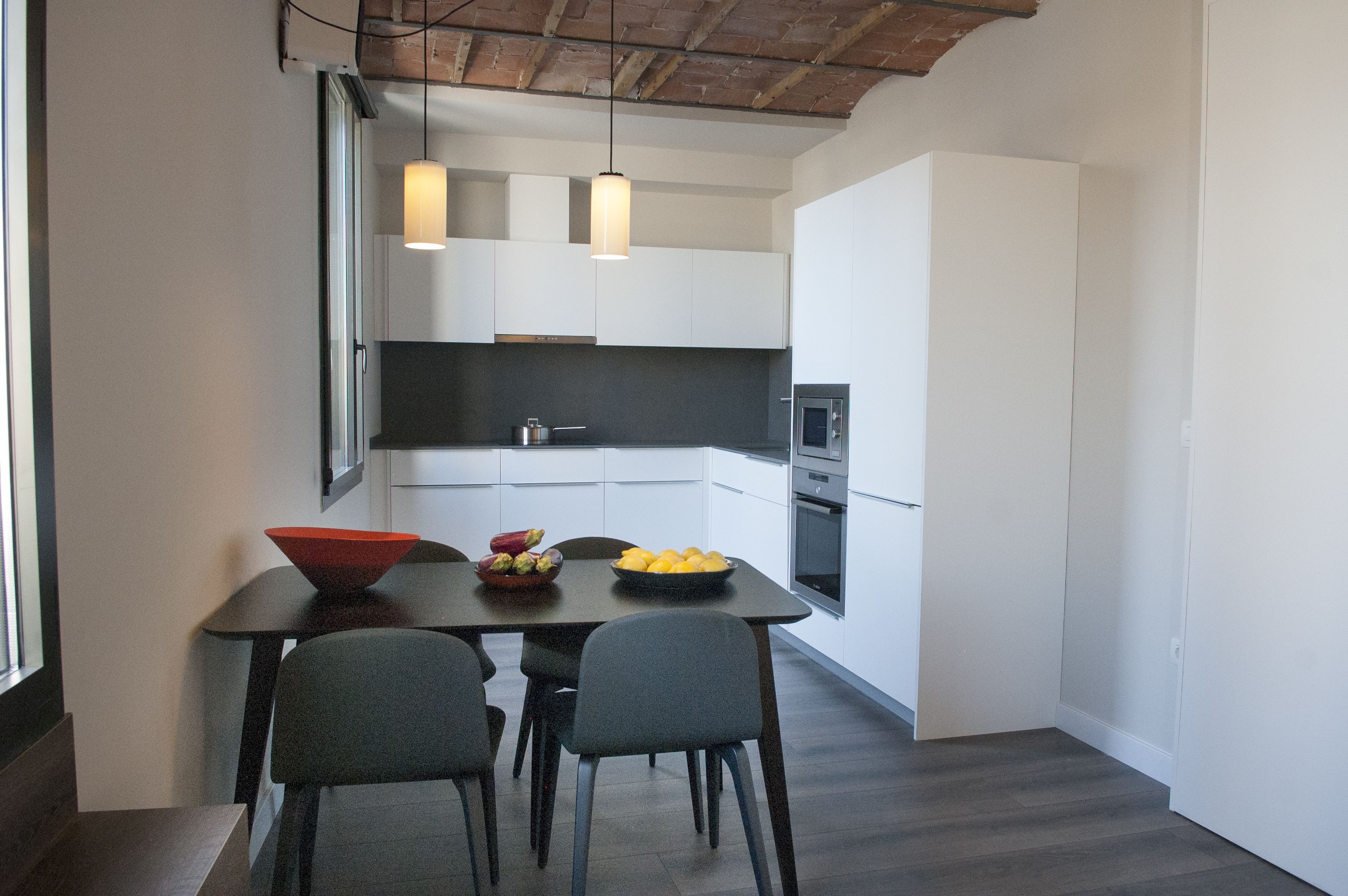 Una cocina moderna con armarios blancos, encimera negra y un comedor con mesa y sillas.
