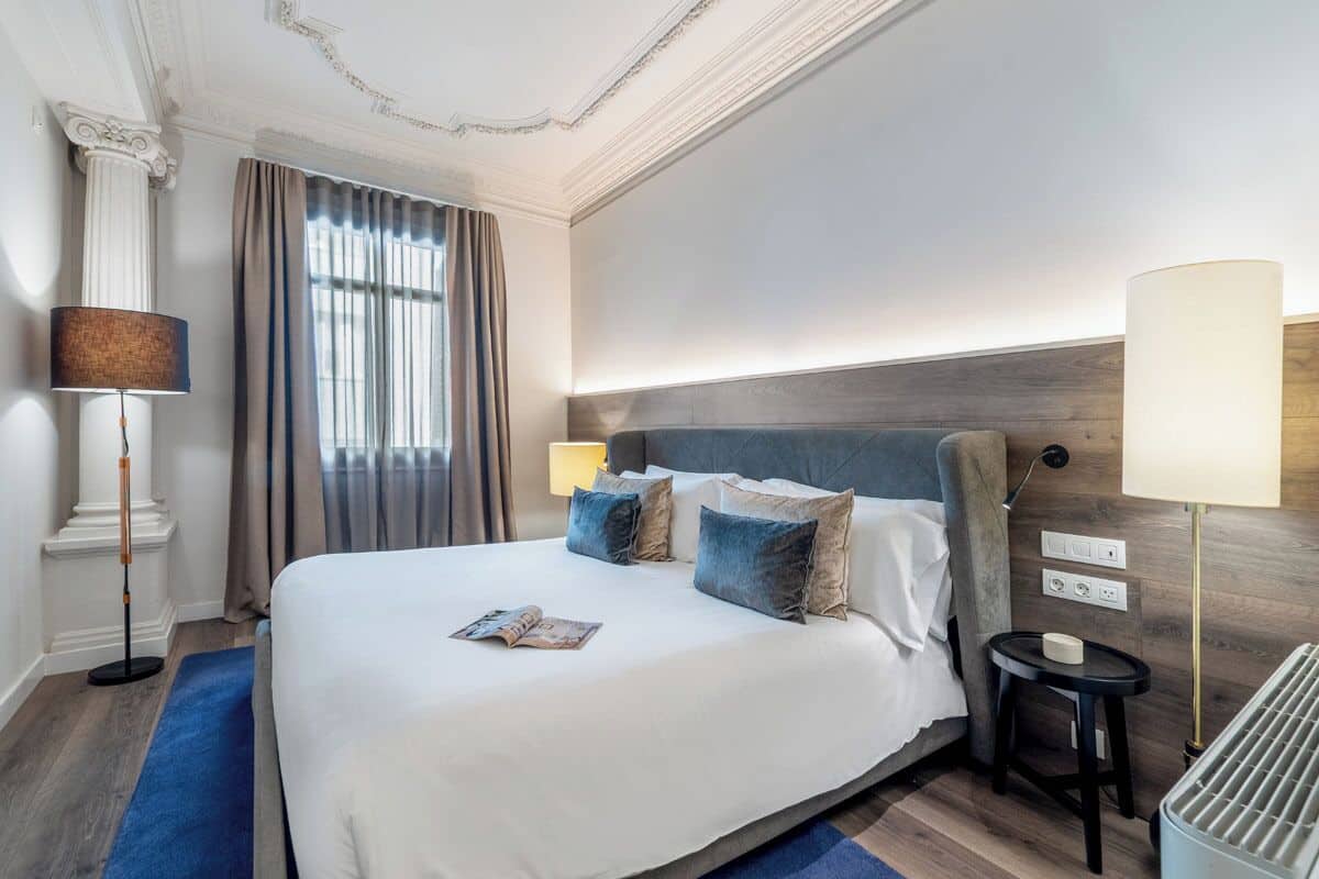 Een hotelkamer met een groot bed, een nachtkastje, een lamp en een raam met gordijnen.