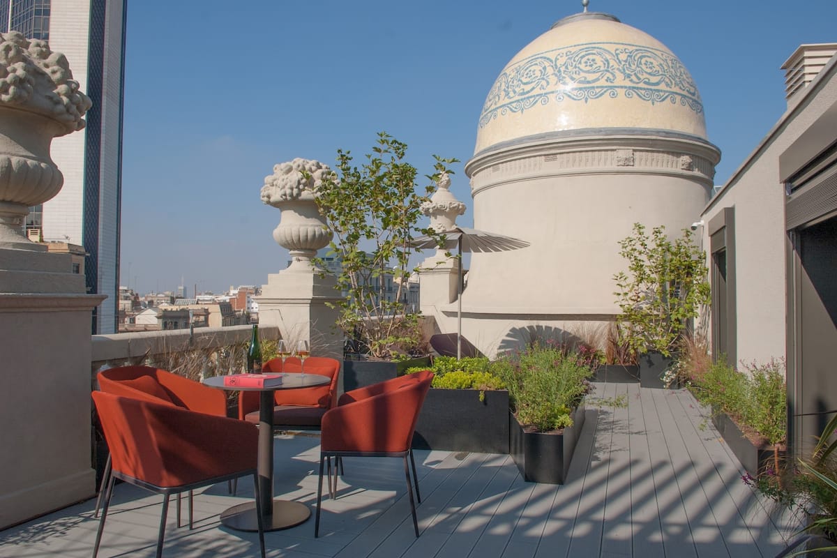 Een terras op het dak met zitplaatsen buiten, decoratieve plantenbakken en een grote koepelconstructie.