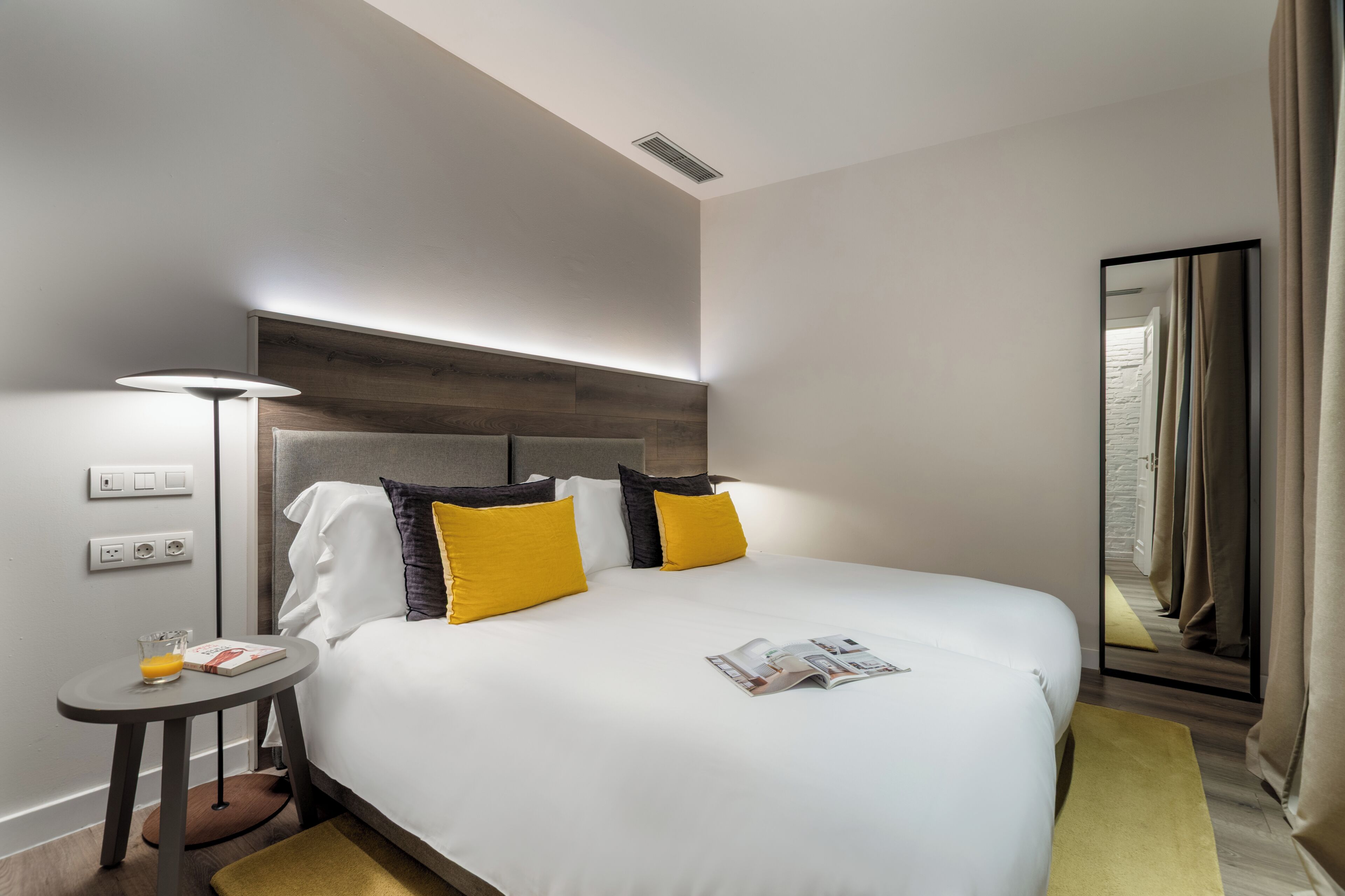 Une chambre d’hôtel moderne avec un grand lit, une table de chevet, une lampe et un miroir.