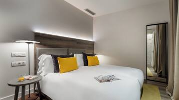 Une chambre d’hôtel moderne avec un grand lit, une table de chevet, une lampe et un miroir.
