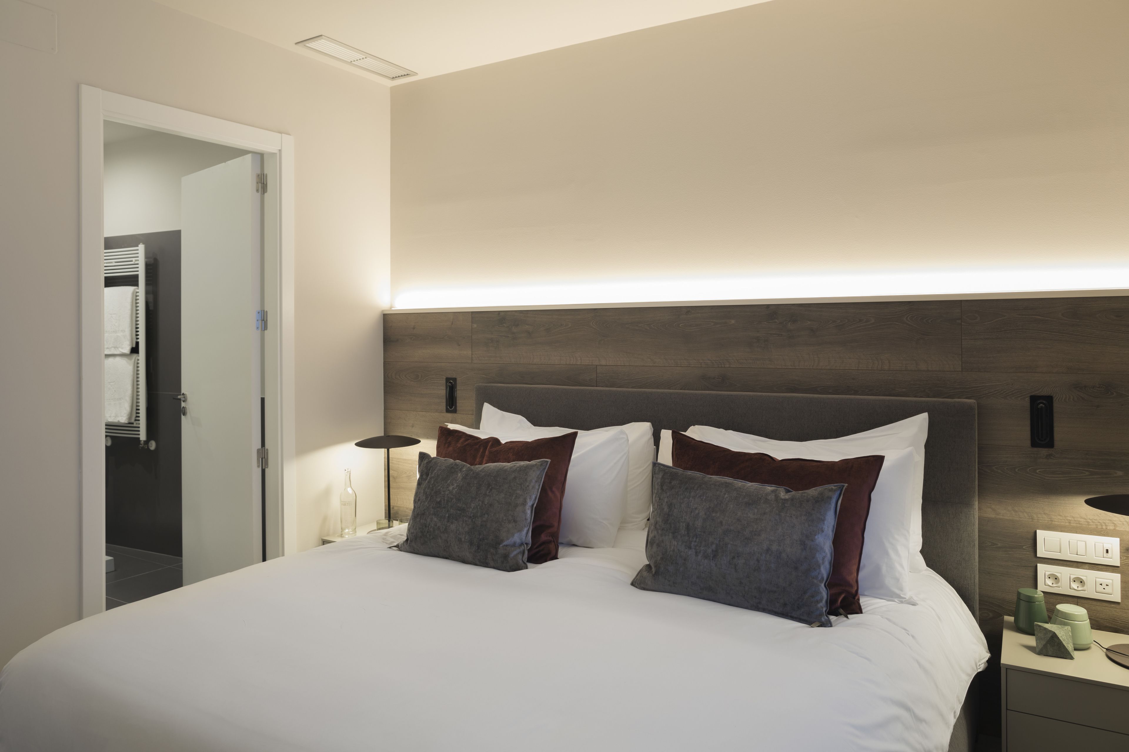 Moderni hotellihuone, jossa on suuri sänky, yöpöytävalaisimet ja puinen pääty.