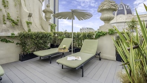 Une terrasse sur le toit avec deux chaises longues, une table avec un panier et un parasol décoratif.