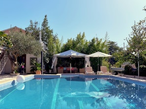 En swimmingpool med ett avskärmat område med sittplatser och solstolar.