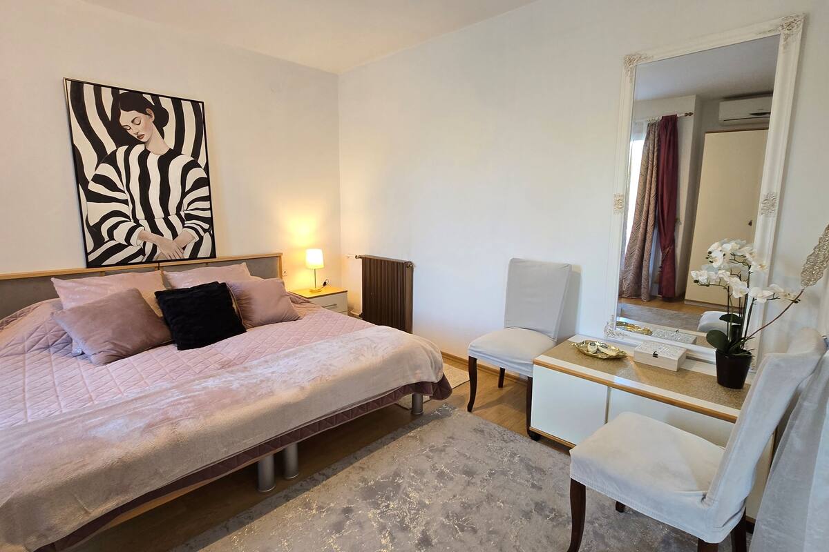 A bedroom with a bed, bedside table, chair, and a large mirror.