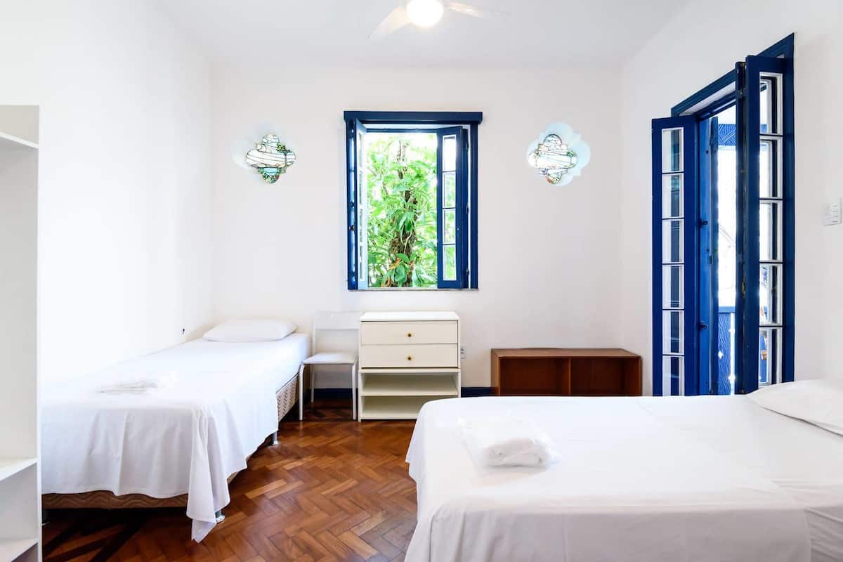 Un dormitorio con dos camas individuales, un escritorio y una silla. Se ve un ventanal con vistas a zonas verdes.