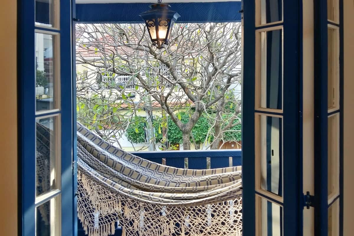 Una hamaca colgada en un balcón con vista a árboles y un edificio al fondo.