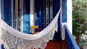 A hammock on a porch with blue shutters, a wooden chair, and a potted plant. - Farfalla Guest House (Rio de Janeiro)