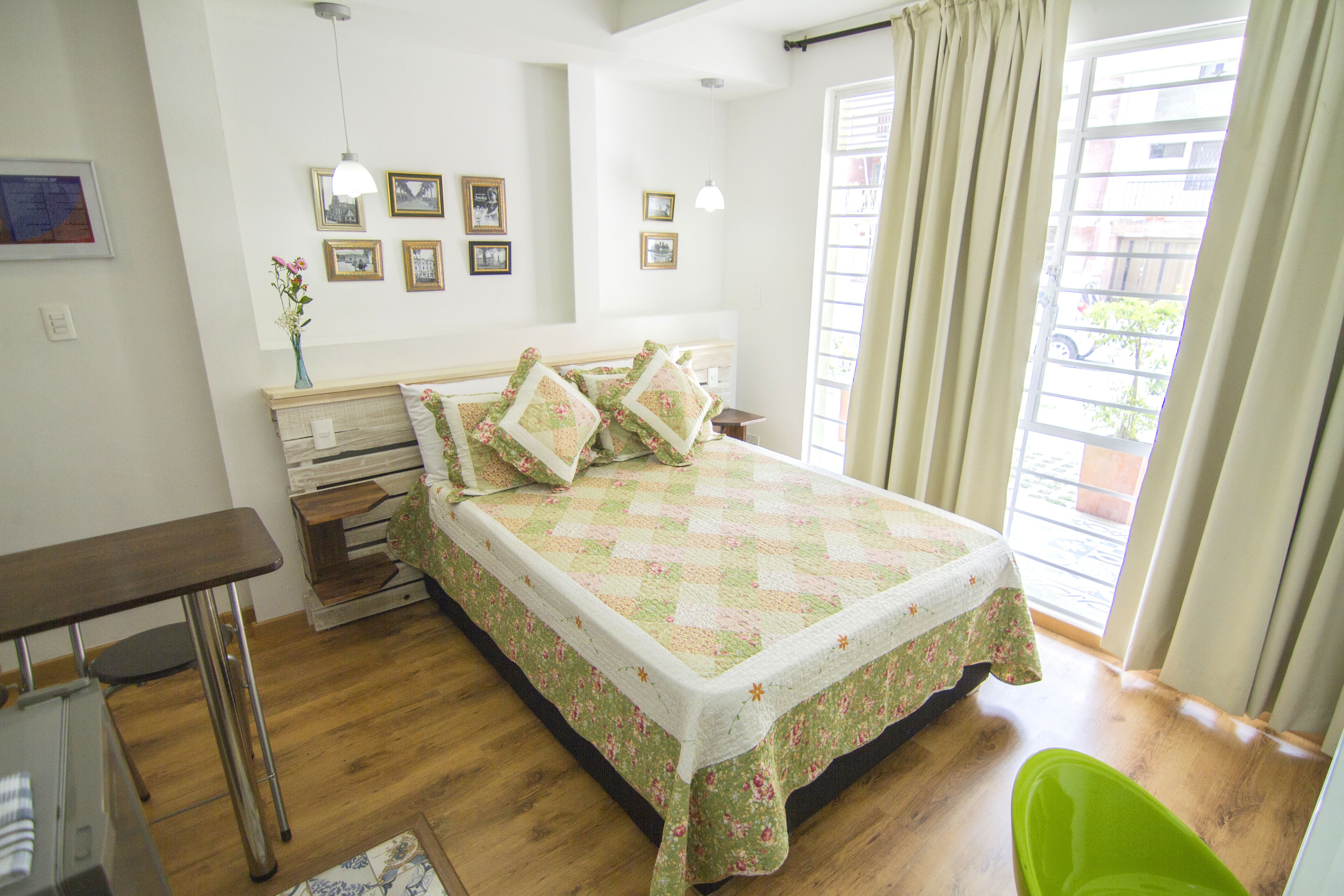 A neatly arranged bedroom with a bed, bedside table, lamp, and a view of the outside through a window.