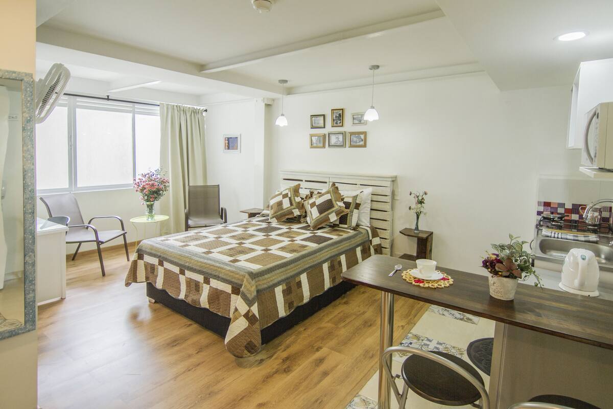 A compact bedroom with a bed, bedside table, and a small desk area.