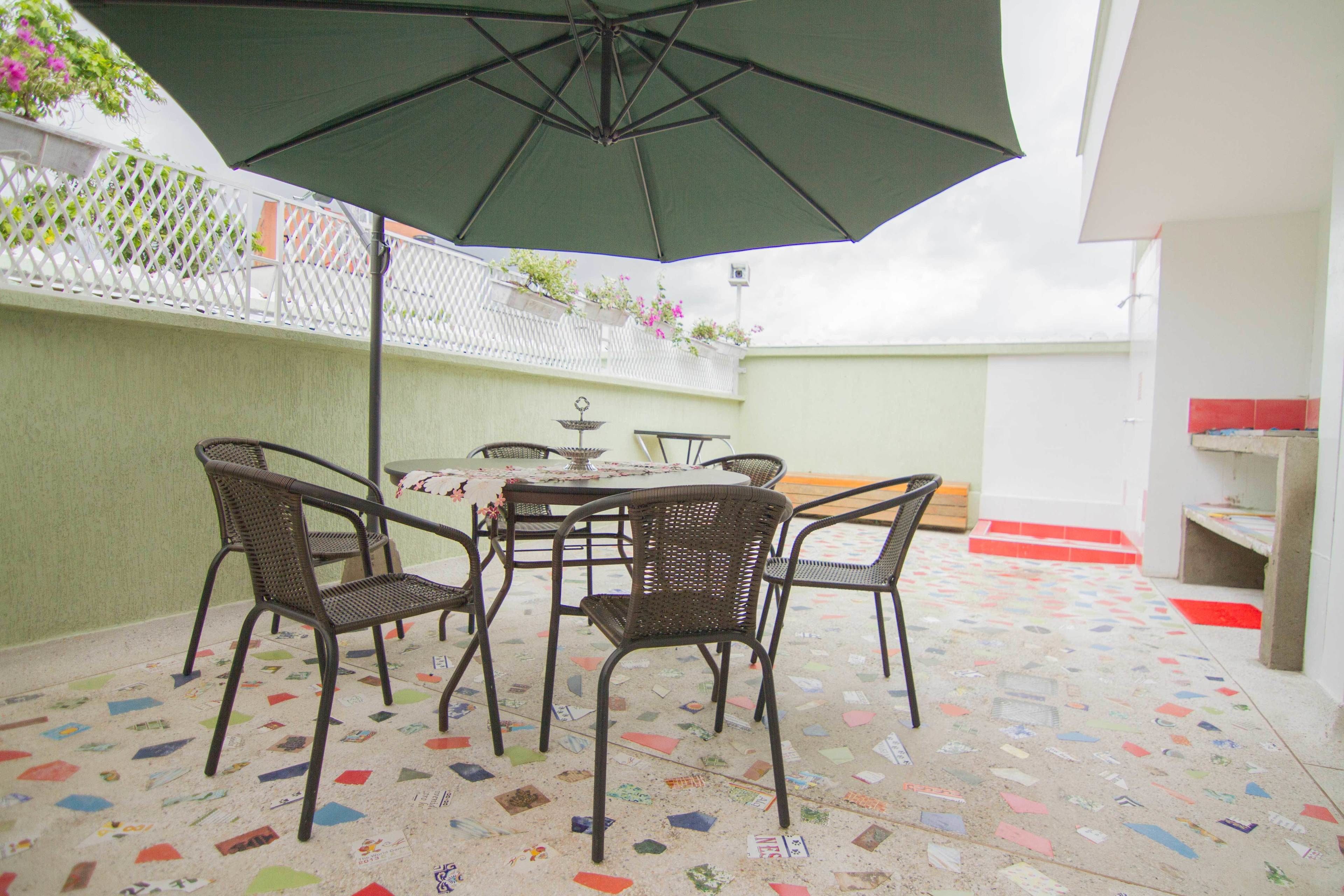 An outdoor patio with a table and chairs, a green umbrella, and a decorative floor.