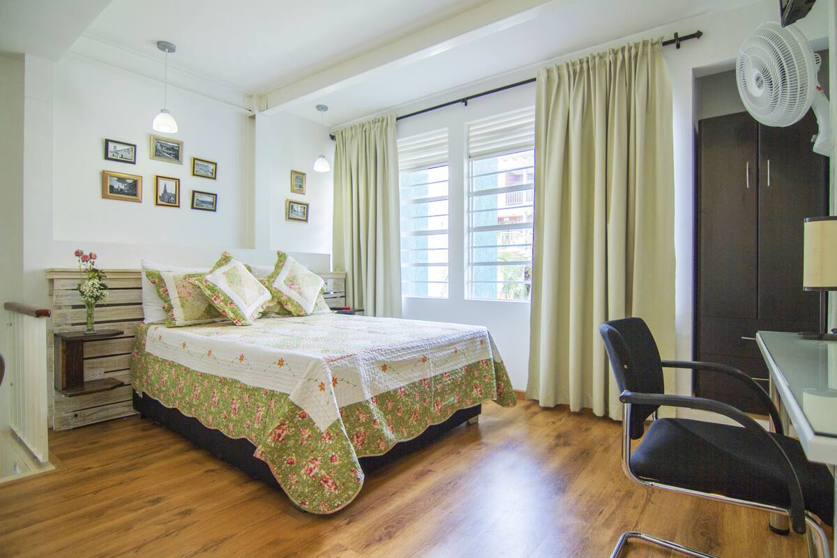 A bedroom with a bed, a chair, a desk, and a window with curtains.
