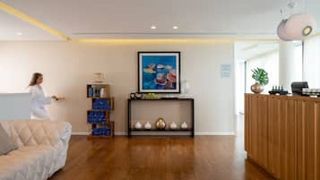 A modern reception area with a wooden reception desk, a console table with decorative items, a blue painting, and a cushioned sofa.