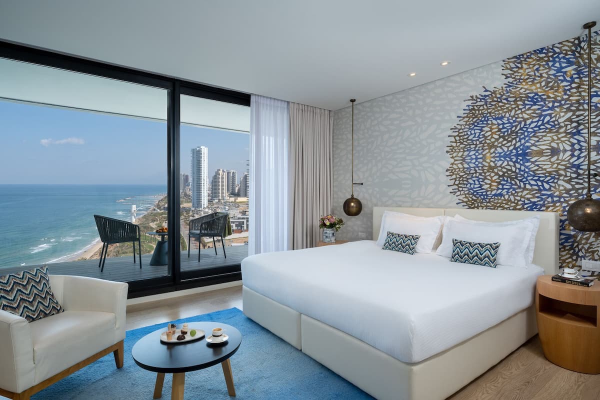A modern hotel room with a large bed, a view of the ocean, and a cityscape.