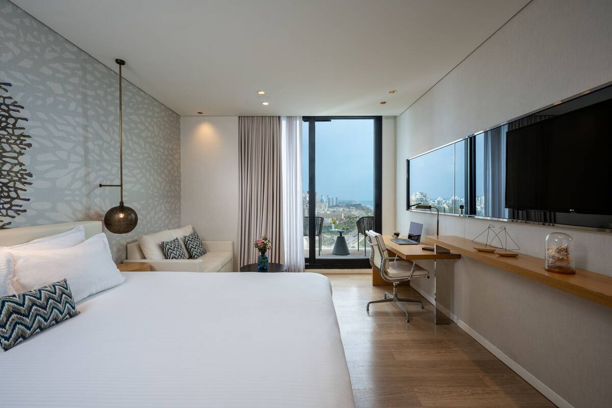A modern hotel room with a large bed, a desk, and a city view.