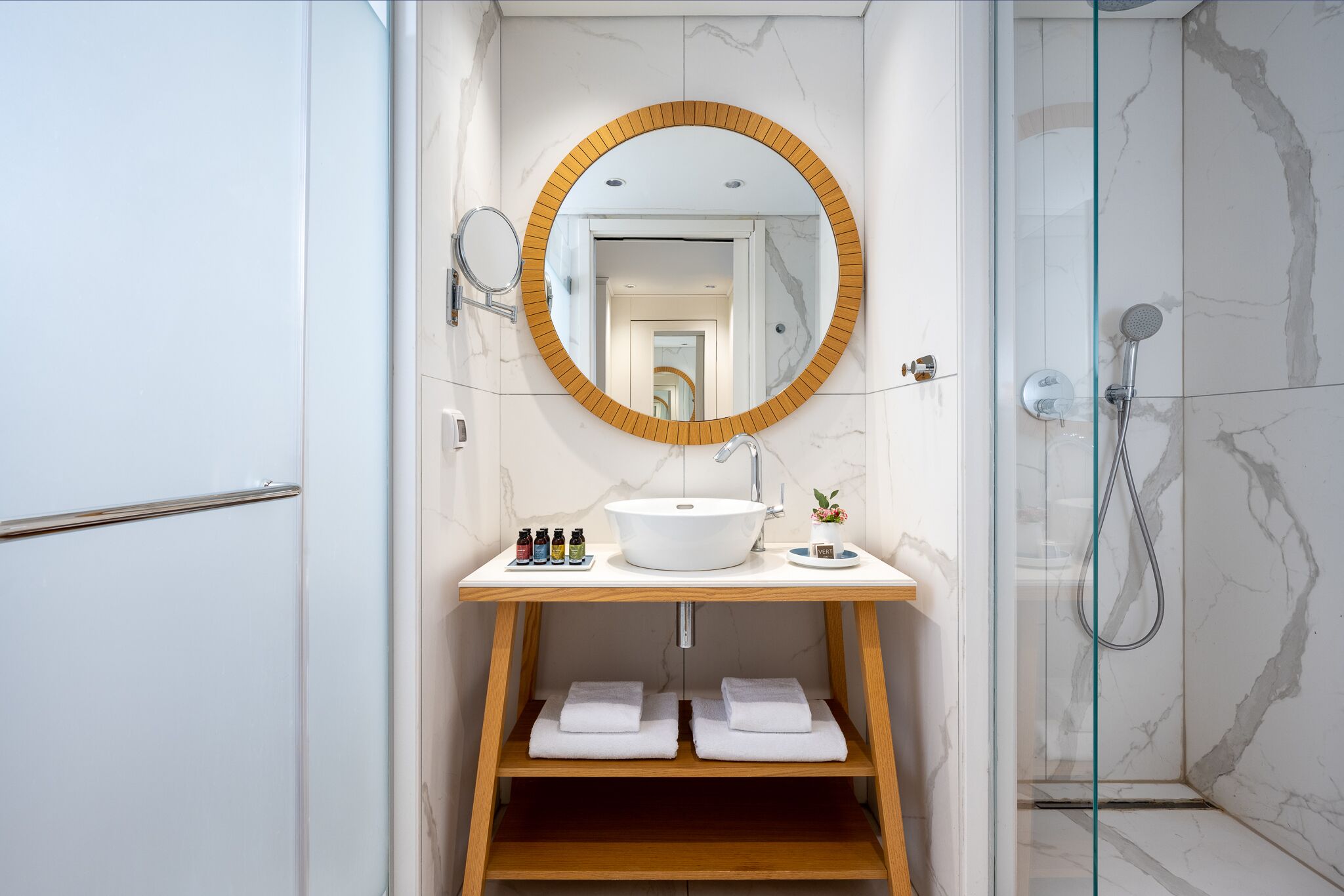 Une salle de bain moderne avec un miroir rond, un lavabo blanc et des étagères en bois.