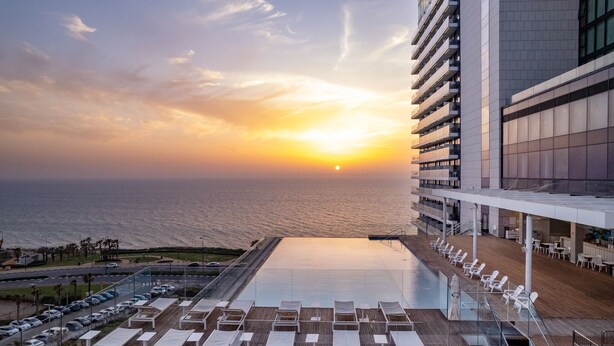 A rooftop pool with lounge chairs and a view of the sunset over the ocean. - Vert Lagoon Netanya By AFI Hotels (Netanya)