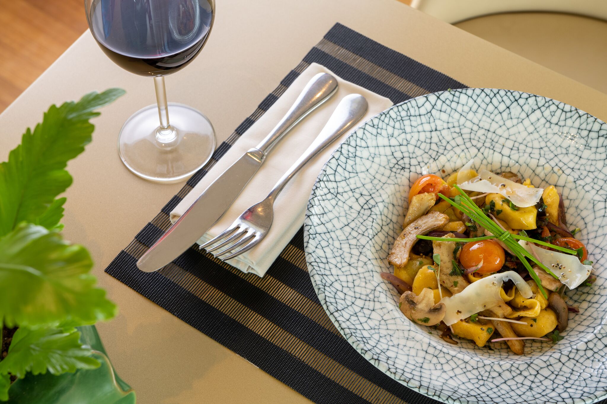 A table setting with a plate of pasta, a glass of red wine, and cutlery.