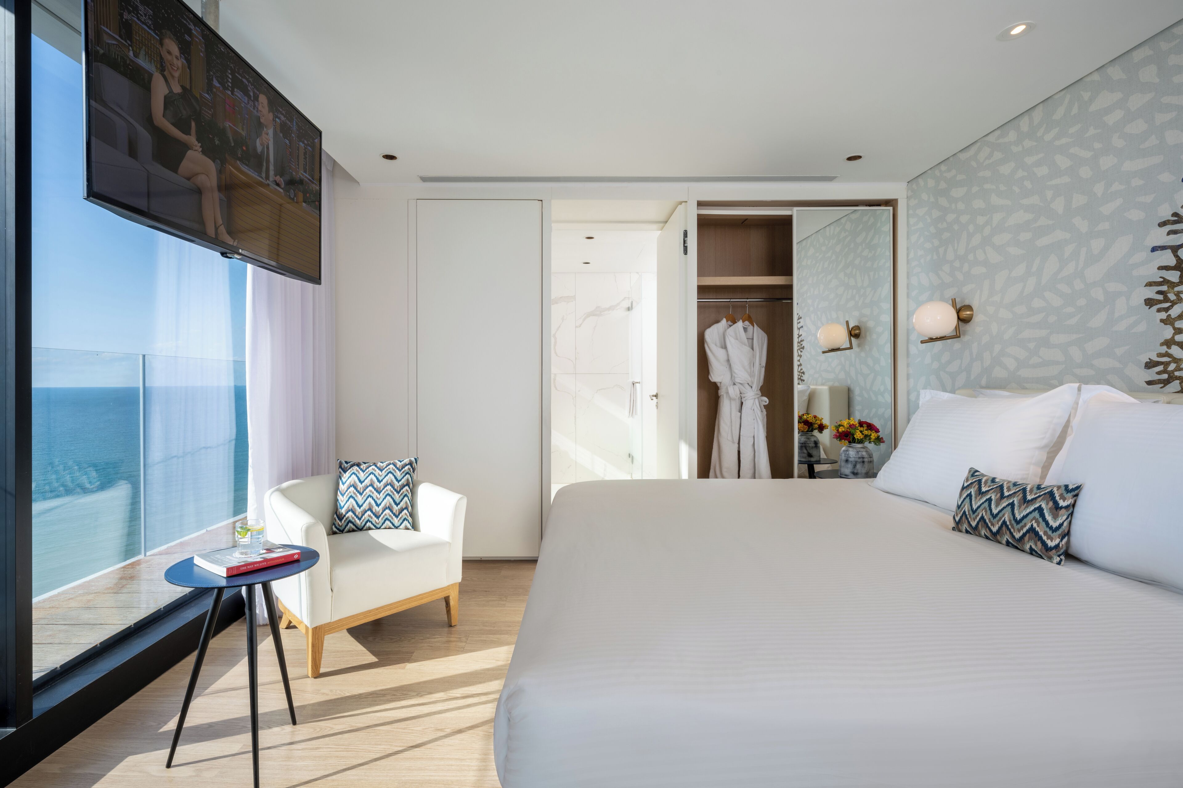 Habitación de hotel moderna con una cama grande, una zona de estar con una mesita pequeña, un armario y un ventanal con vistas.