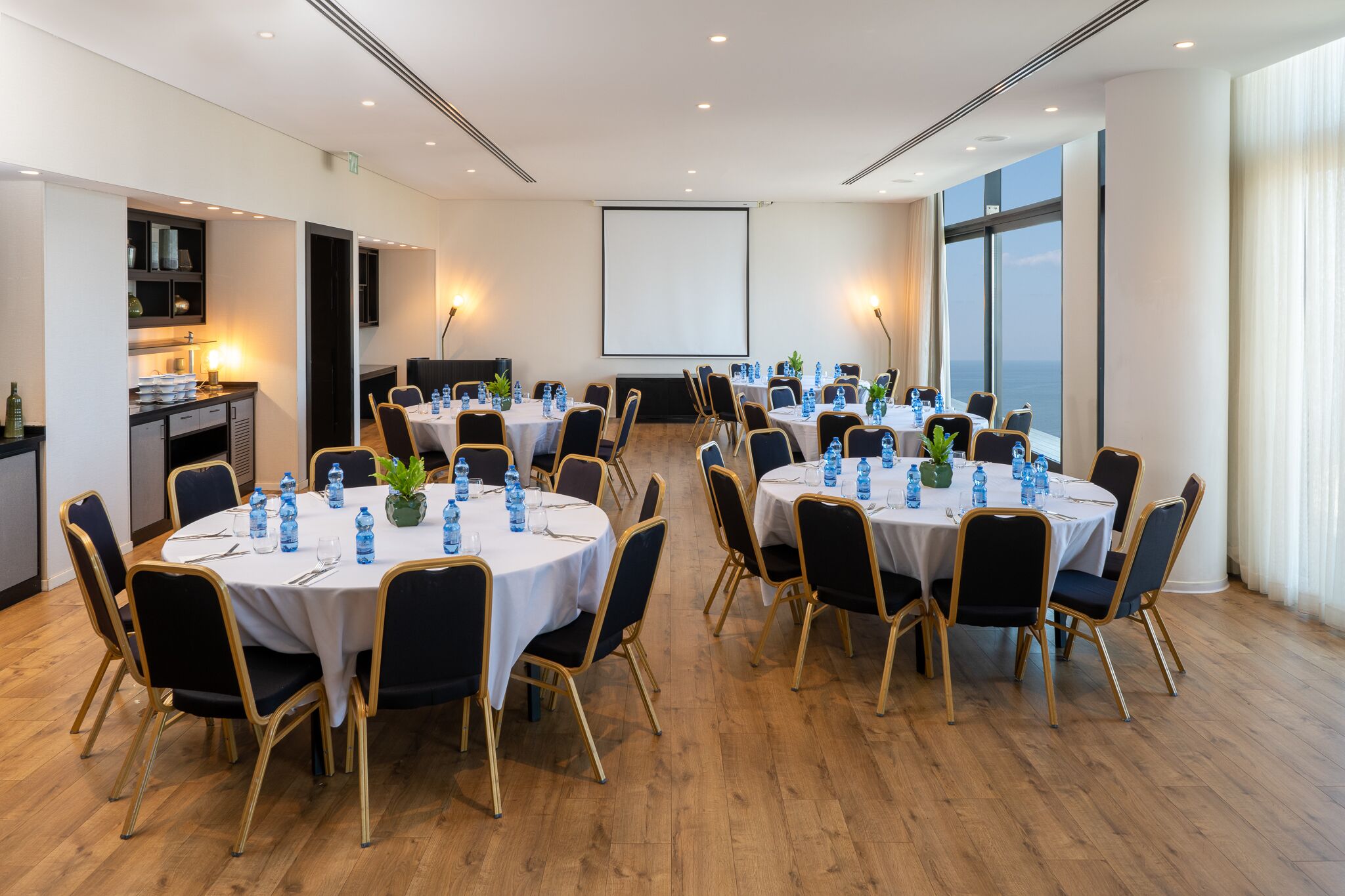 A conference room with round tables, chairs, and a projector screen.