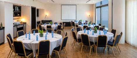A conference room with round tables, chairs, and a projector screen.