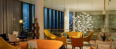 Un vestíbulo moderno con diversas opciones de asiento, incluyendo sofás y sillones, y un amplio ventanal que ofrece vistas de la ciudad.