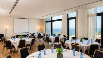 A conference room with round tables, chairs, water bottles, and a projector screen.