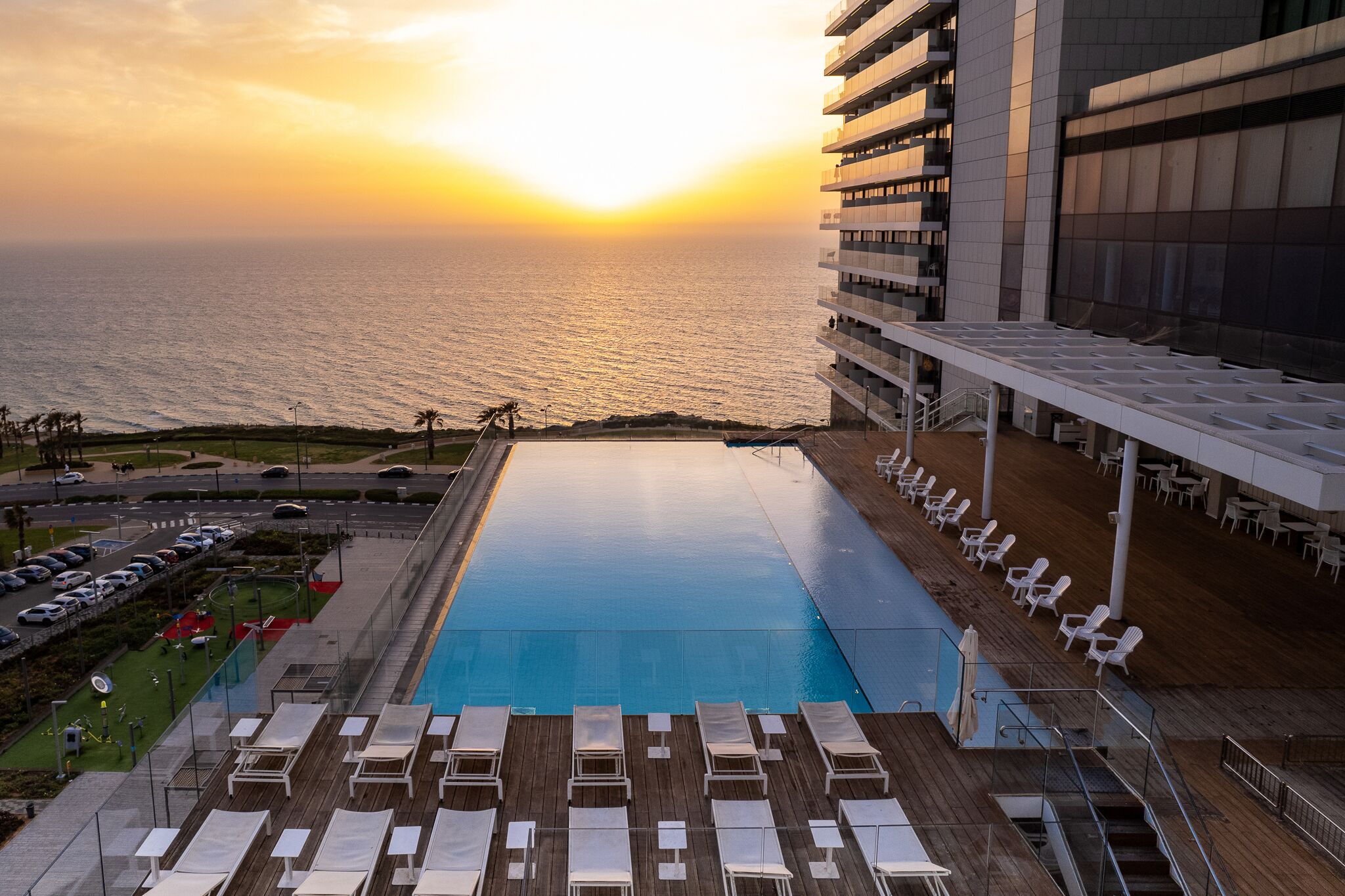 Una piscina en la azotea con sillones de descanso, vistas al océano y un edificio moderno con balcones.