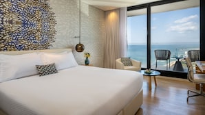 A modern hotel room with a large bed, a view of the sea, and a dining area with chairs and a table. - Vert Lagoon Netanya By AFI Hotels (Netanya)