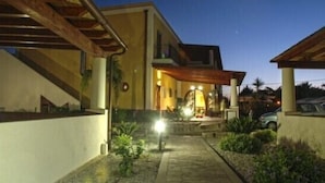 A modern building with a covered patio area, a stone pathway, and a well-lit entrance. - Eolian Residence (Lipari)
