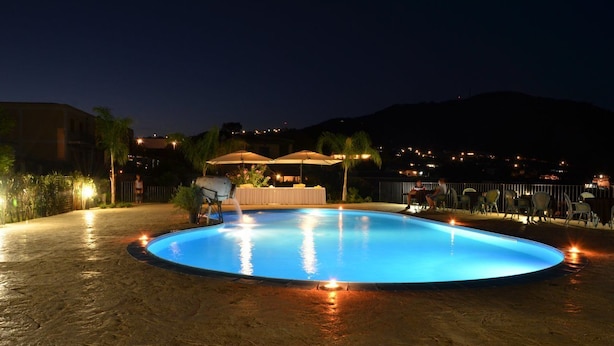 A swimming pool with a sunken center, surrounded by chairs and umbrellas, with a view of a hillside and distant buildings. - Eolian Residence (Lipari)