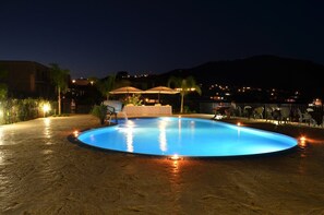 A swimming pool with a sunken center, surrounded by chairs and umbrellas, with a view of a hillside and distant buildings. - Eolian Residence (Lipari)