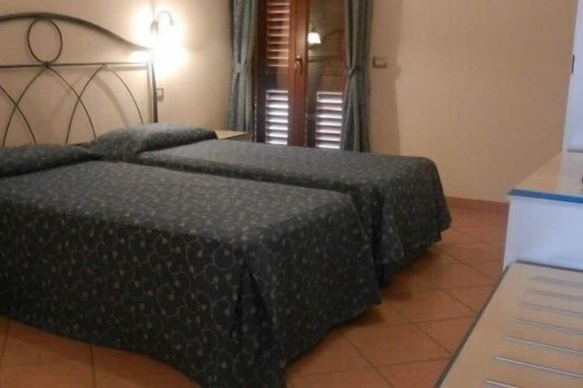 A room with two beds, a nightstand, and a desk with a chair.