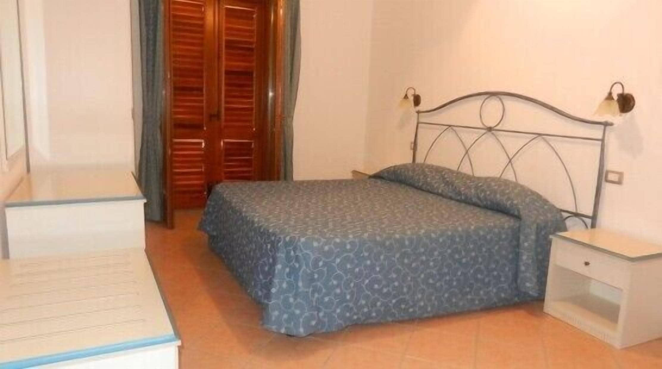 Un dormitorio con una cama, una mesita de noche, un armario de madera y un escritorio.