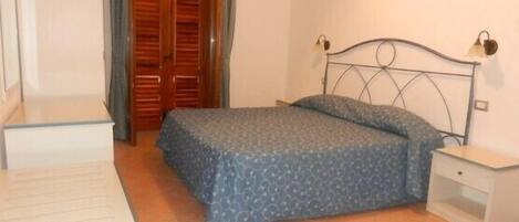Un dormitorio con una cama, una mesita de noche, un armario de madera y un escritorio.