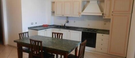A compact kitchen with white cabinets, a black countertop, and a dining table with chairs.