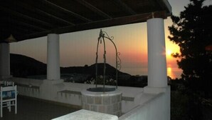 A covered outdoor area with a stone fountain, white columns, and a sunset view. - Eolian Residence (Lipari)