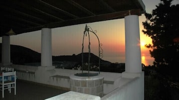 Un espacio al aire libre techado con una fuente de piedra, columnas blancas y vistas al atardecer.