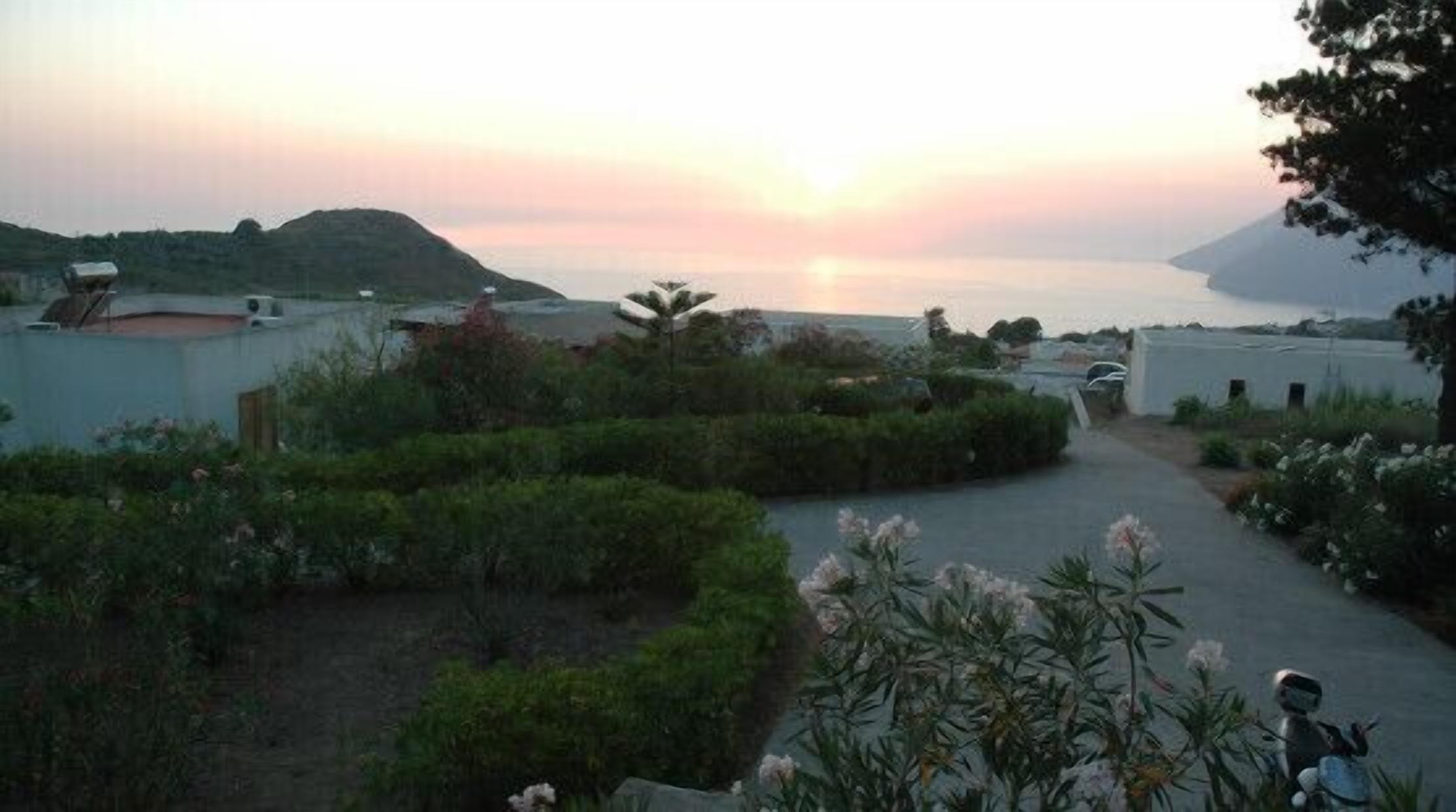 A residential area with a curved pathway, greenery, and a sunset over a body of water.