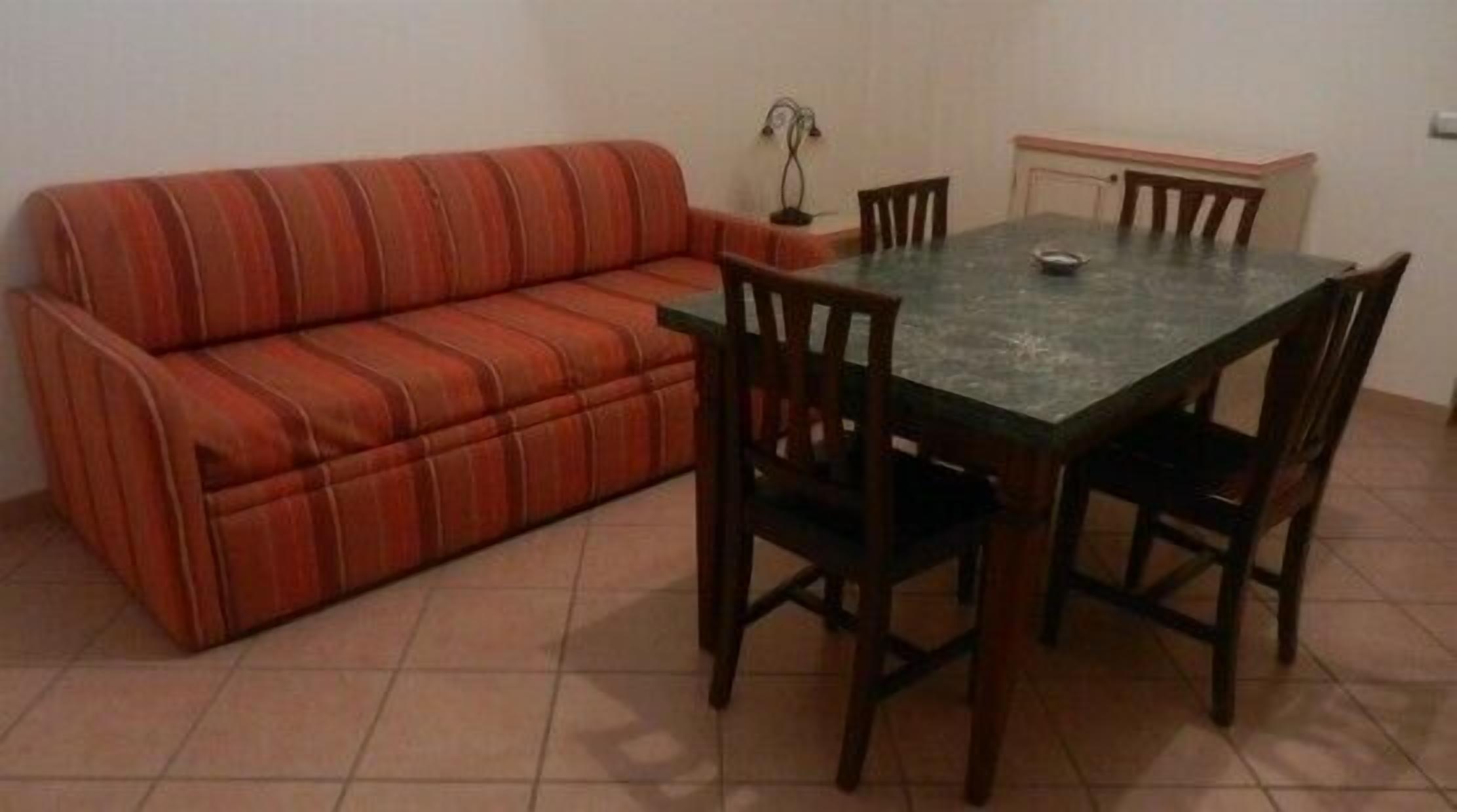 A room with a striped sofa, a dining table with chairs, and a cabinet.