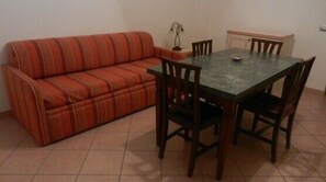 A room with a striped sofa, a dining table with chairs, and a cabinet. - Eolian Residence (Lipari)