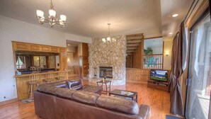 A spacious living area with a stone fireplace, leather sofa, wooden flooring, and a large TV. - 569 Lucerne 4 Bedroom Home by RedAwning (South Lake Tahoe)