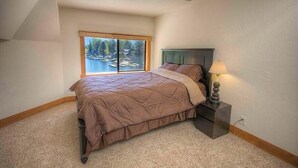 A bedroom with a large window, a bed, a nightstand with a lamp, and a view of a lake. - 569 Lucerne 4 Bedroom Home by RedAwning (South Lake Tahoe)