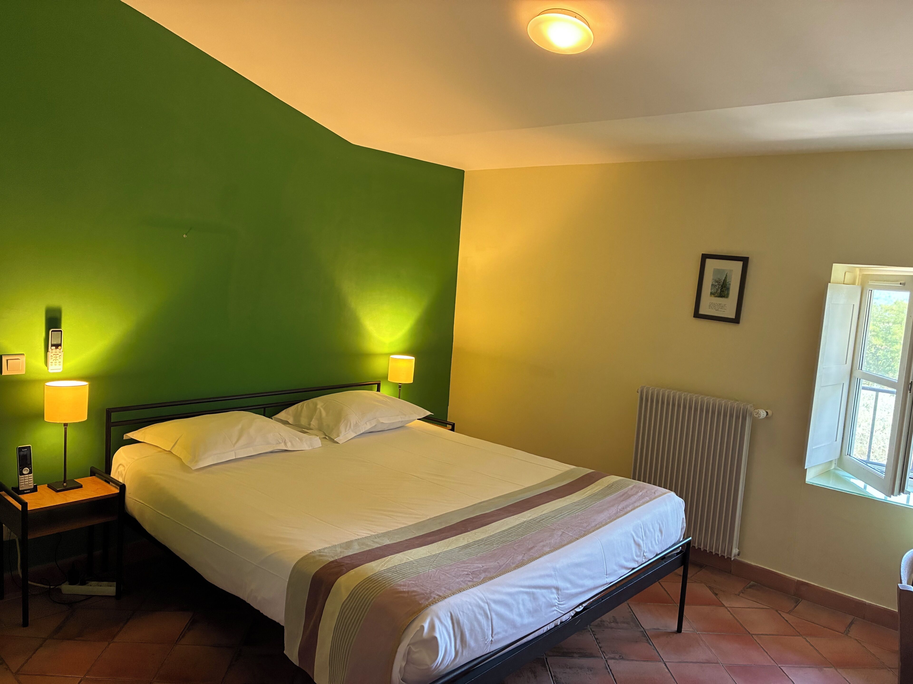 A room with a bed, two bedside lamps, a radiator, and a window.