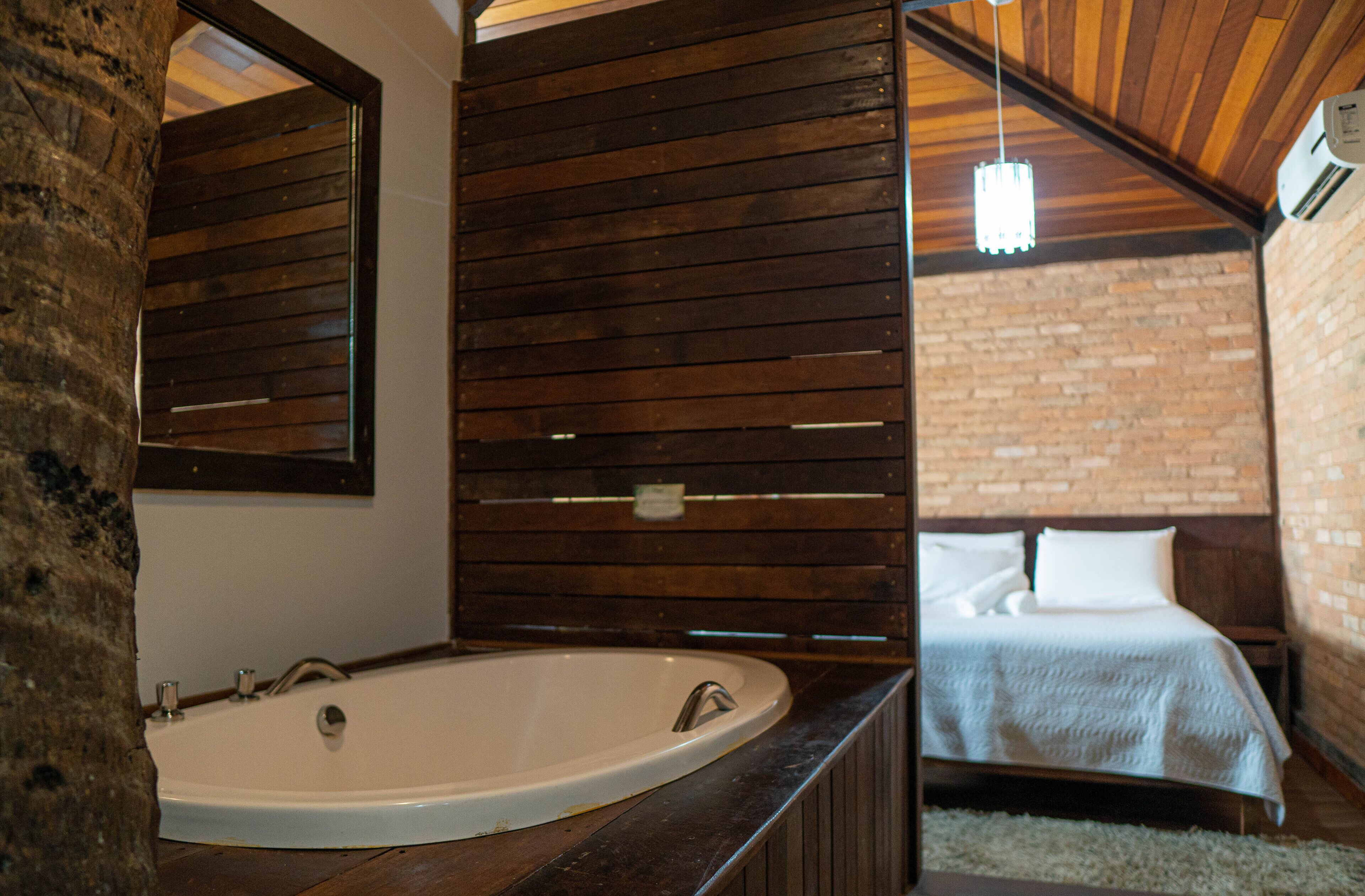 Uma casa de banho com uma banheira grande, ripas de madeira na parede e uma cama no quarto adjacente.
