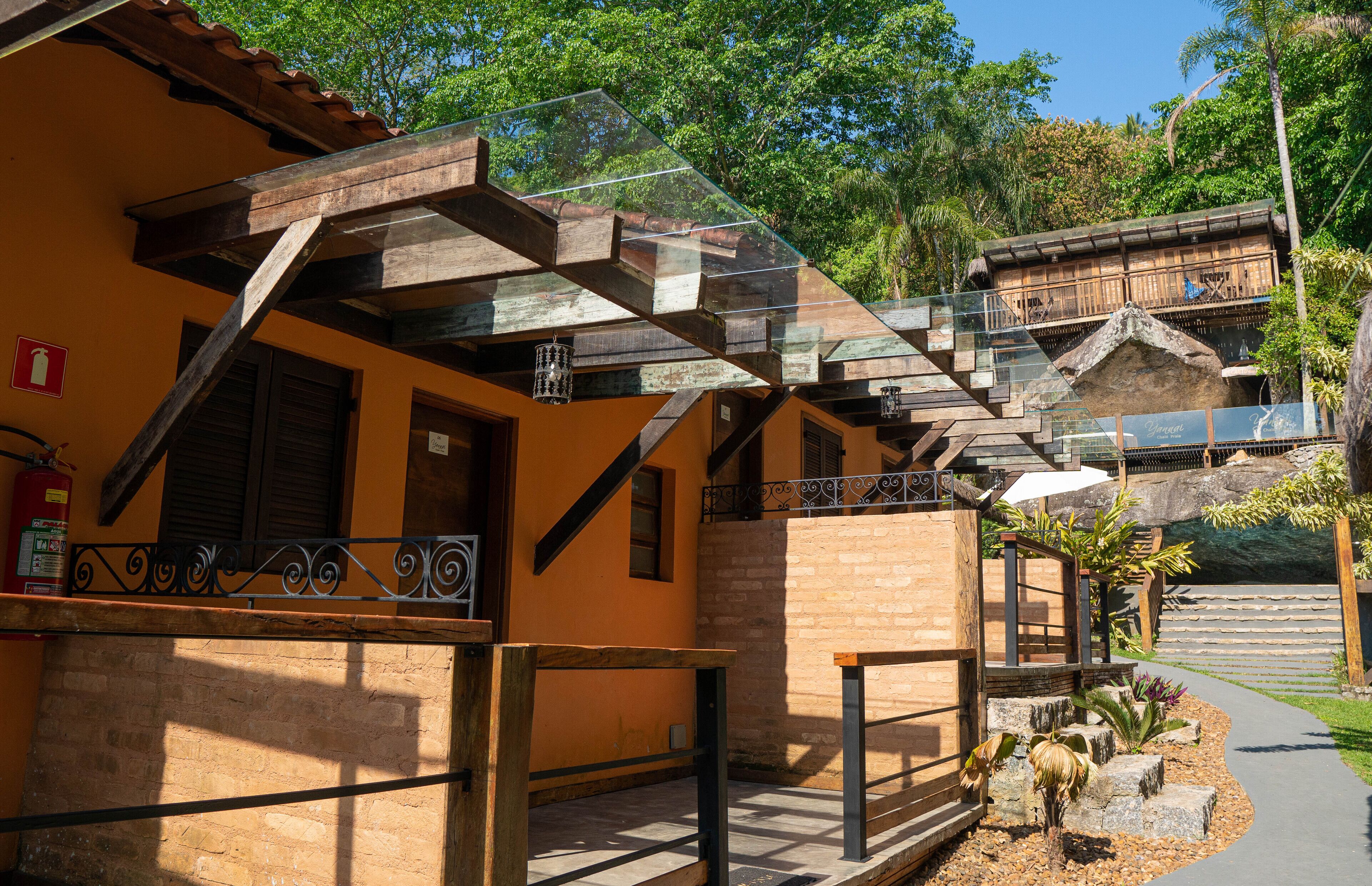 A building with a wooden staircase, a balcony with a metal railing, and a stone pathway leading to a seating area.