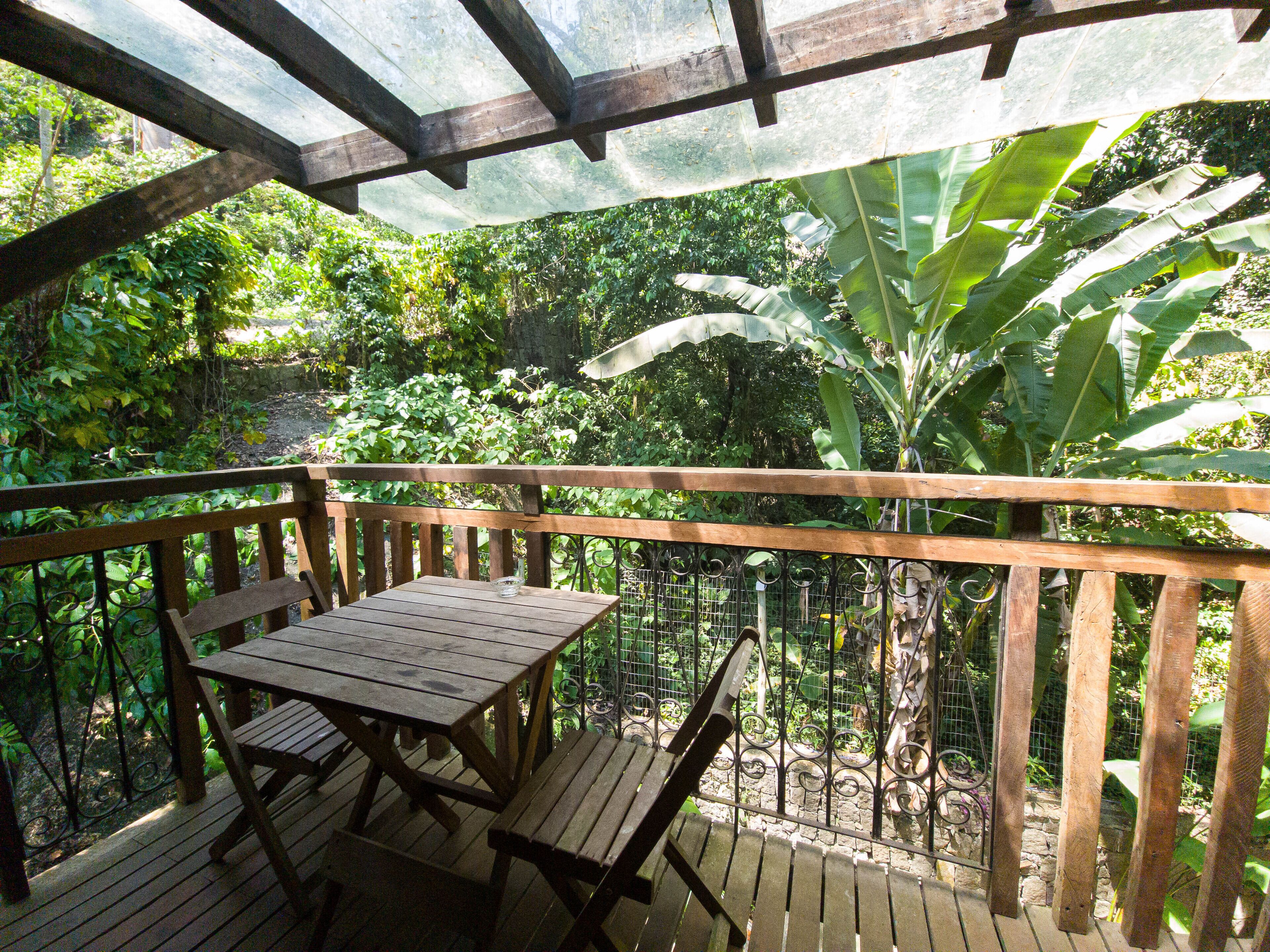 Une terrasse en bois avec une table et des chaises, entourée d’une végétation luxuriante et d’une clôture en métal.