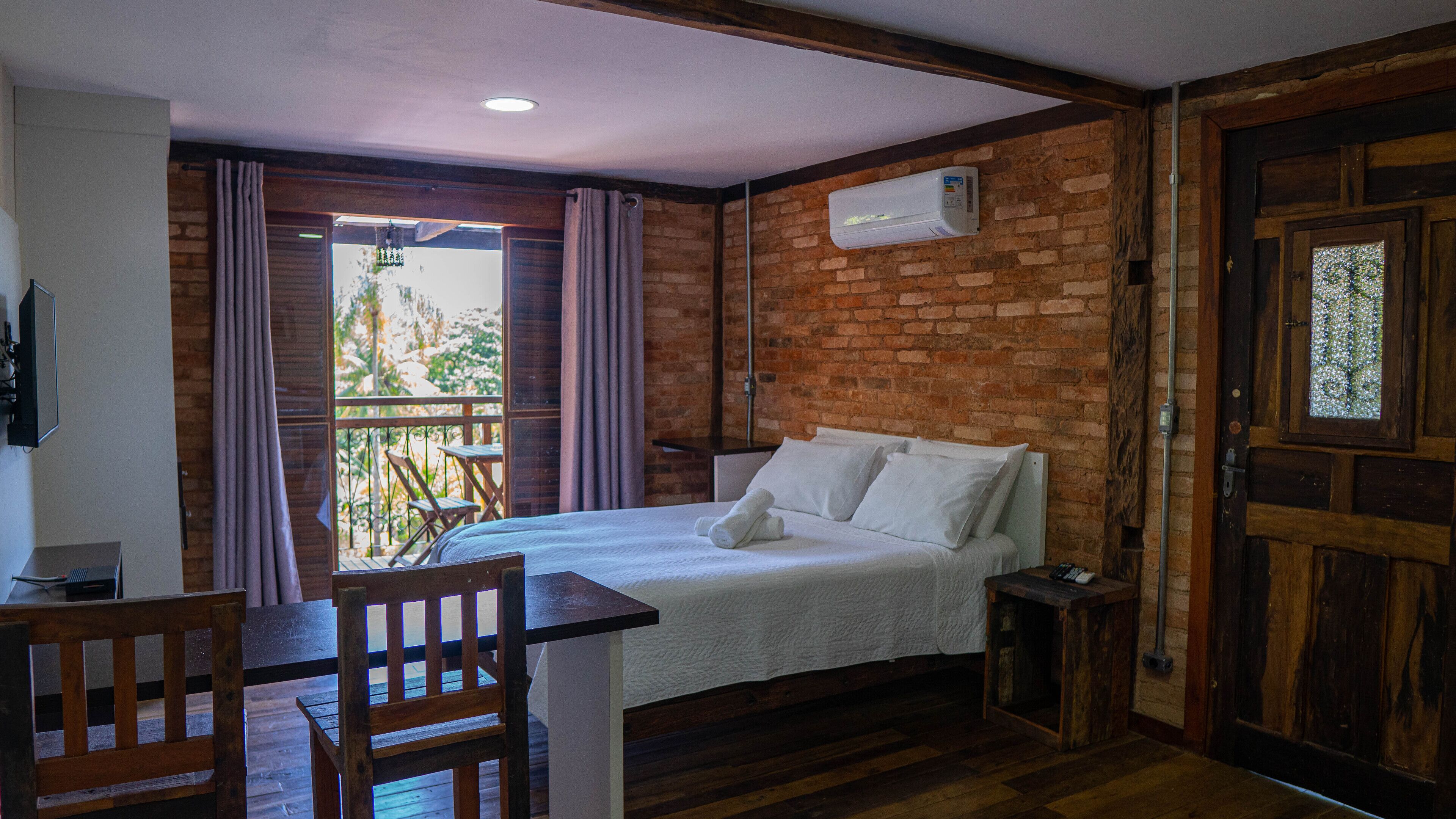 A bedroom with a bed, a desk, a chair, a window with curtains, and a brick wall.